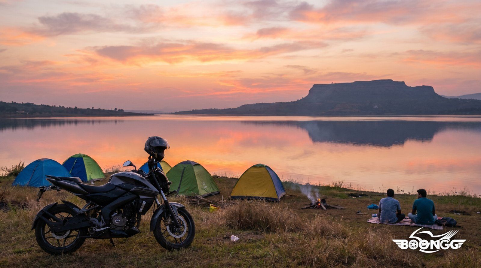 Motorcycle parked beside Pawna Lake at sunset with camping tents and Lohagad fort silhouette