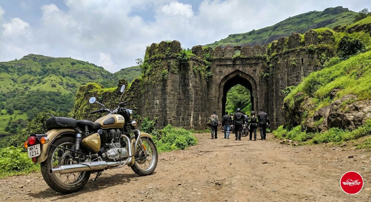 Royal Enfield parked at Sinhagad Fort entrance with stone fortification and green hills